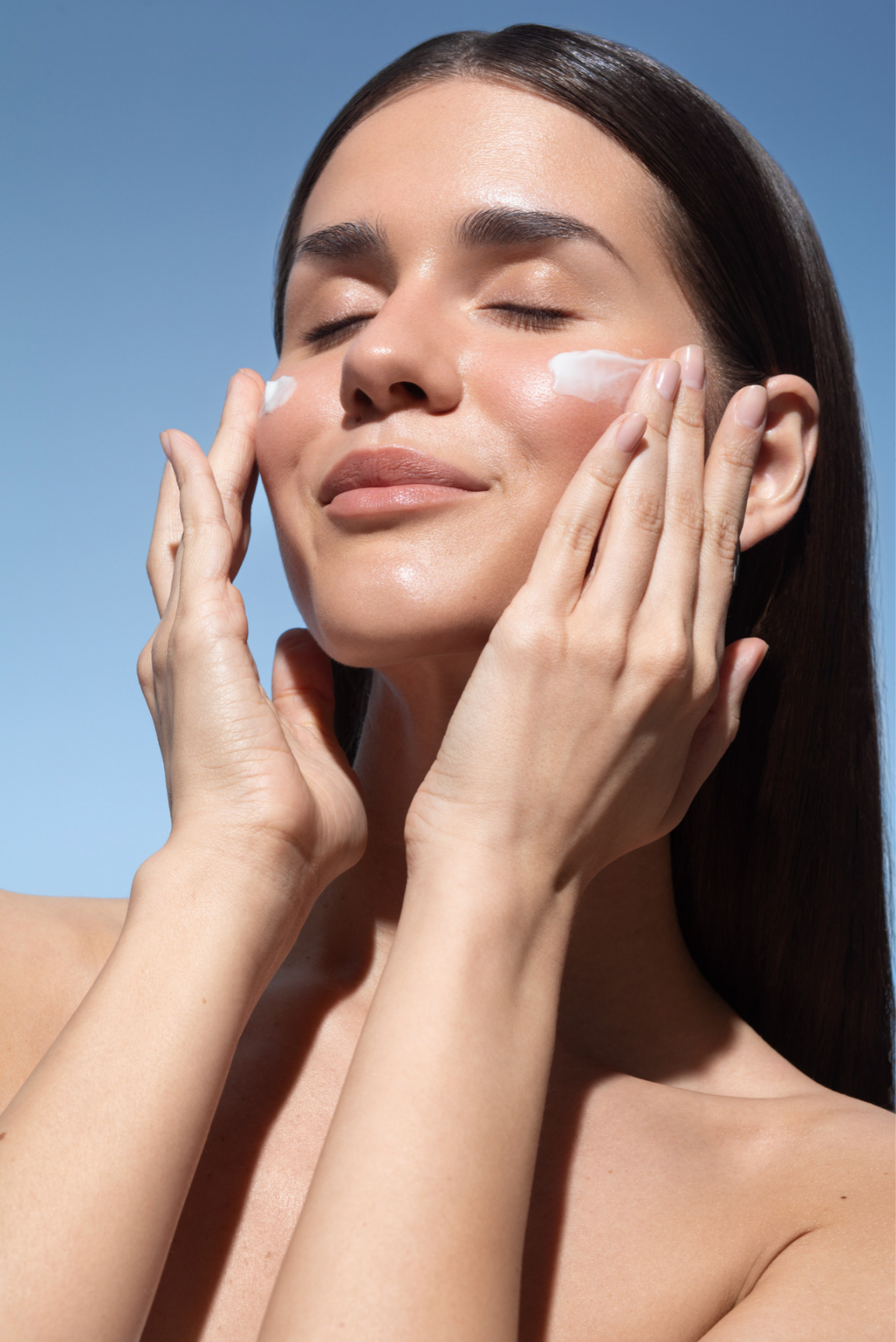 Woman applying Blanchard Skincare moisturizer to her face outdoors against a blue sky